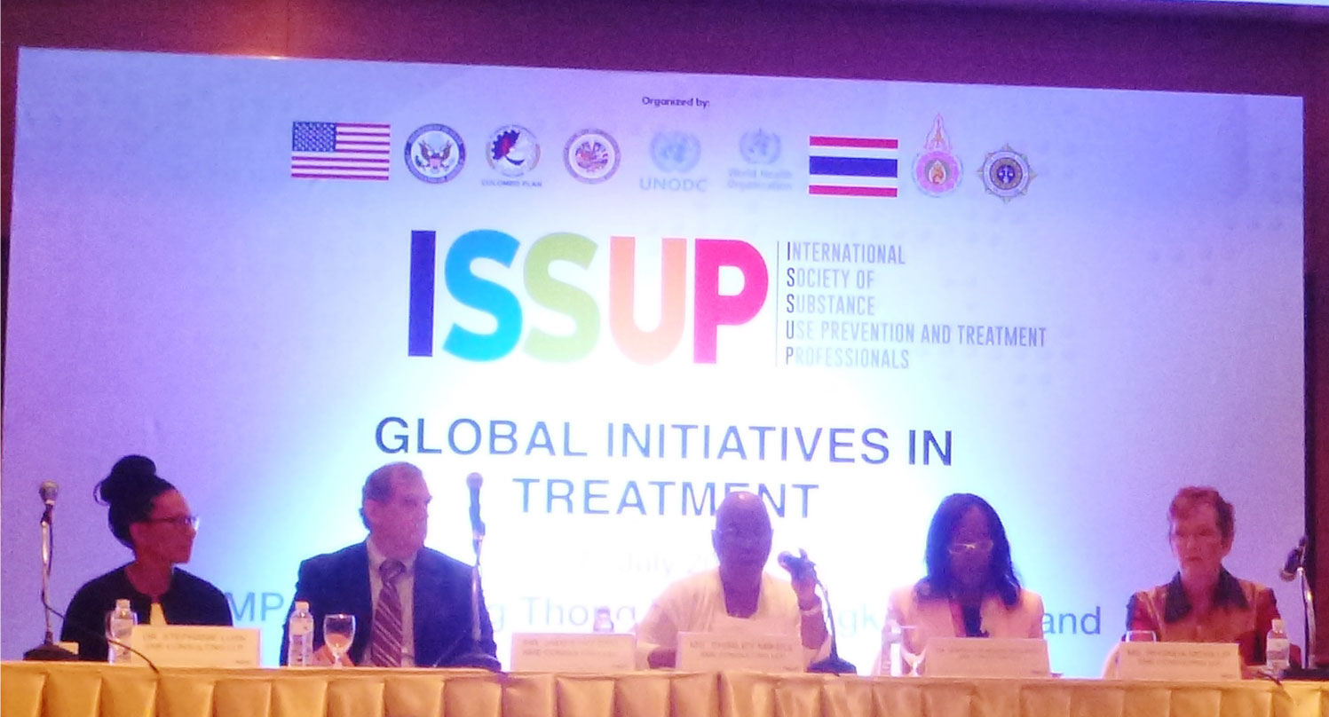 A group of people sitting at a table in front of a sign that says isup global initiatives in treatment.